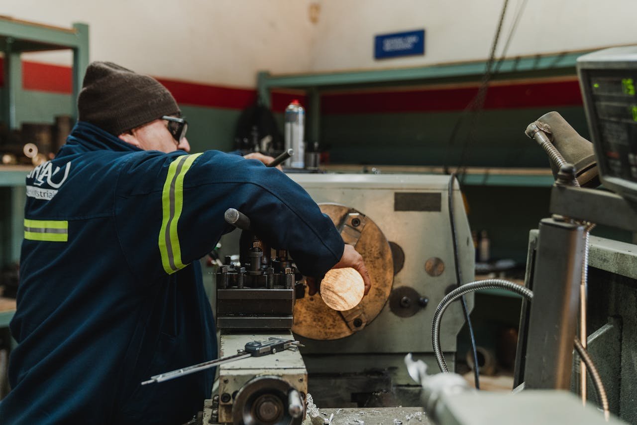 Industrial worker focused on operating a lathe in a busy workshop setting.